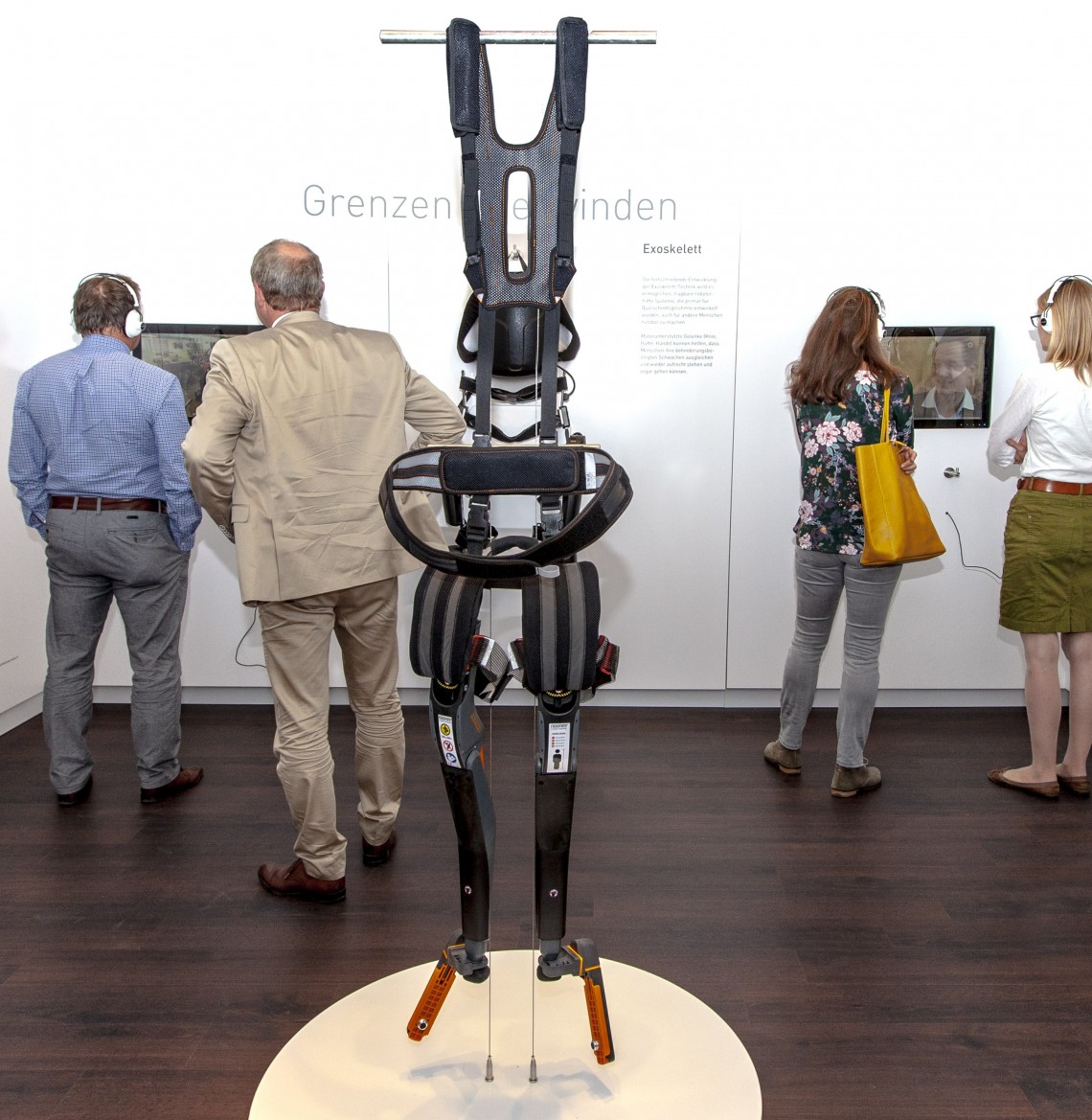 Blick in den Ausstellungsraum mit verschiedenen Exoskeletten und Besucherinnen und Besuchern beim Betrachten der Exponate