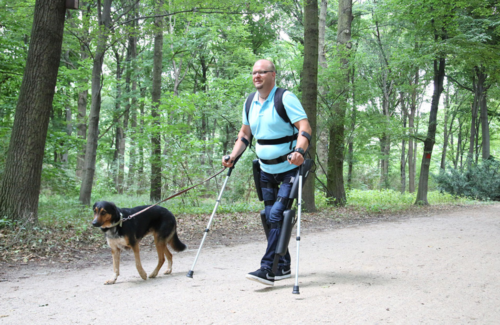 Ein Mann mit angelegtem ReWalk-Exoskelett geht mit seinem Hund im Wald spazieren.
